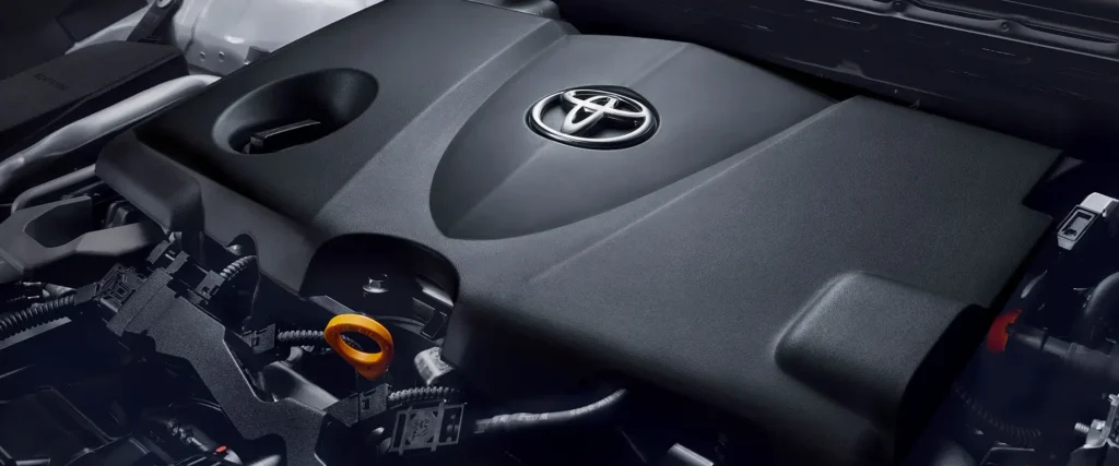 Toyota engine bay showing branded motor cover with chrome logo and various automotive components underneath