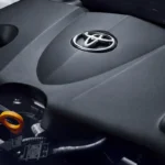 Toyota engine bay showing branded motor cover with chrome logo and various automotive components underneath