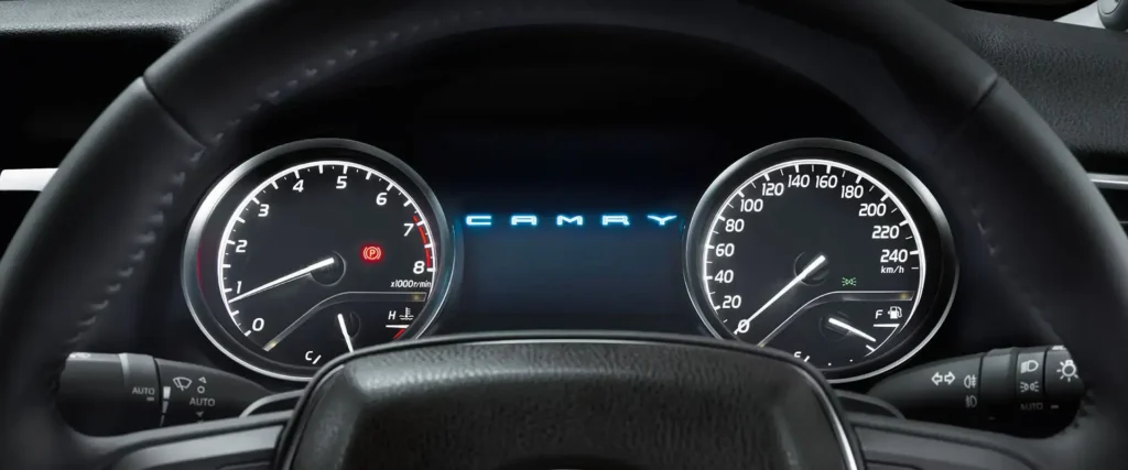 Driver view of Toyota Camry dashboard gauges displaying rpm meter and speedometer with steering wheel logo visible