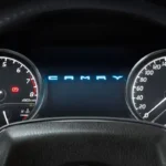 Driver view of Toyota Camry dashboard gauges displaying rpm meter and speedometer with steering wheel logo visible
