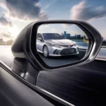 Side mirror view showing Toyota Camry sedan on highway with urban landscape and dramatic cloudy sky reflection