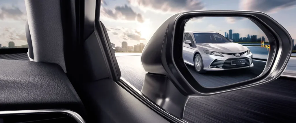 Side mirror view showing Toyota Camry sedan on highway with urban landscape and dramatic cloudy sky reflection