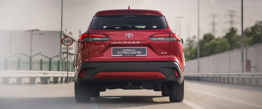 Red Toyota Corolla Cross rear view on highway showing SUV proportions and Cross badging with infrastructure
