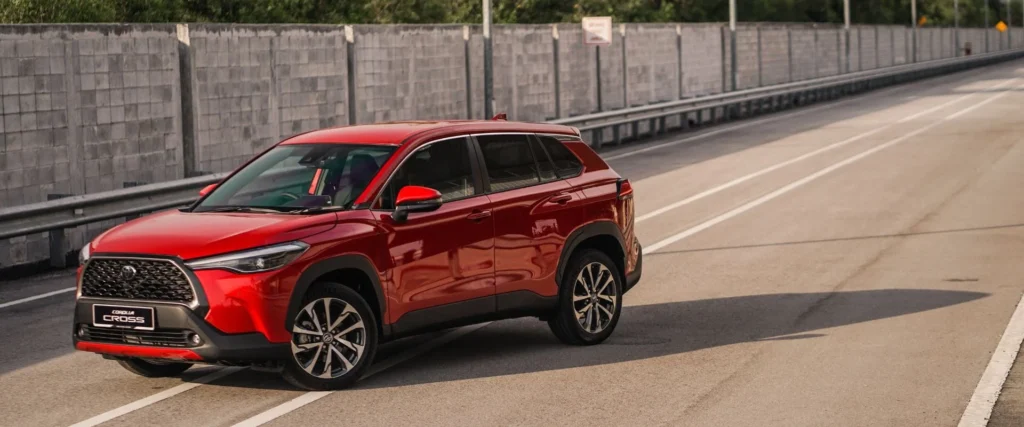 Red Toyota Corolla Cross driving on highway with modern urban infrastructure and concrete safety barriers