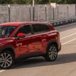 Red Toyota Corolla Cross driving on highway with modern urban infrastructure and concrete safety barriers