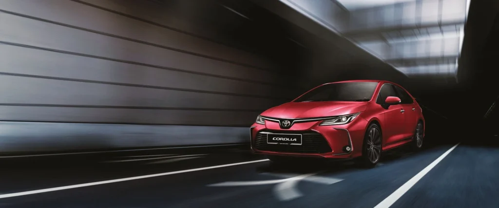 Red Toyota Corolla sedan parked in modern underground garage with dramatic lighting and concrete architecture