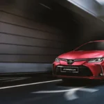 Red Toyota Corolla sedan parked in modern underground garage with dramatic lighting and concrete architecture