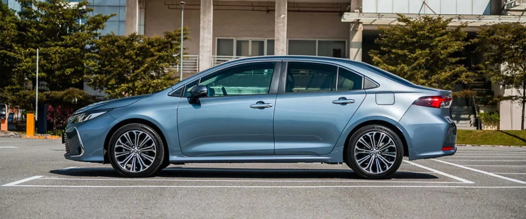 Blue Toyota Corolla profile view parked outside modern office building with glass facade and urban landscaping