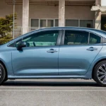 Blue Toyota Corolla profile view parked outside modern office building with glass facade and urban landscaping