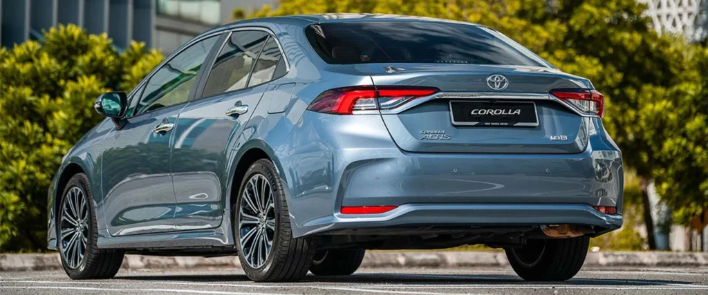 Toyota Corolla sedan positioned against modern urban skyline with glass buildings and green landscaping