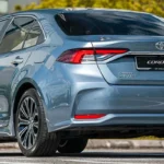 Toyota Corolla sedan positioned against modern urban skyline with glass buildings and green landscaping