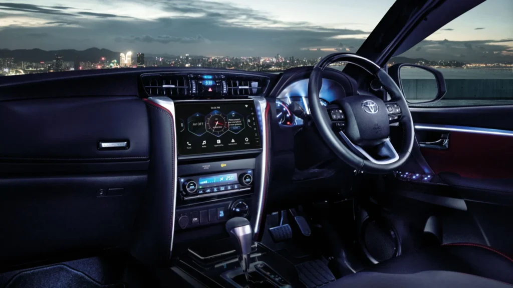 Toyota Fortuner interior dashboard view with infotainment system and illuminated city skyline through windshield
