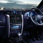 Toyota Fortuner interior dashboard view with infotainment system and illuminated city skyline through windshield