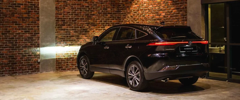 Black Toyota Harrier SUV parked in industrial garage with exposed brick walls and sleek alloy wheel design
