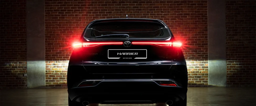 Toyota Harrier rear view with illuminated LED taillights and HARRIER badge against dramatic brick wall setting