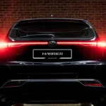 Toyota Harrier rear view with illuminated LED taillights and HARRIER badge against dramatic brick wall setting