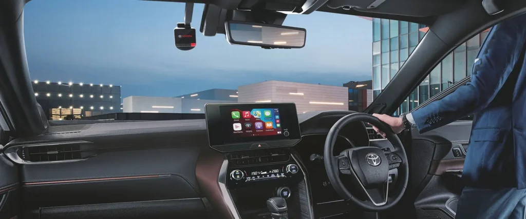 Toyota Harrier interior with driver using multimedia system displaying various app icons and navigation interface
