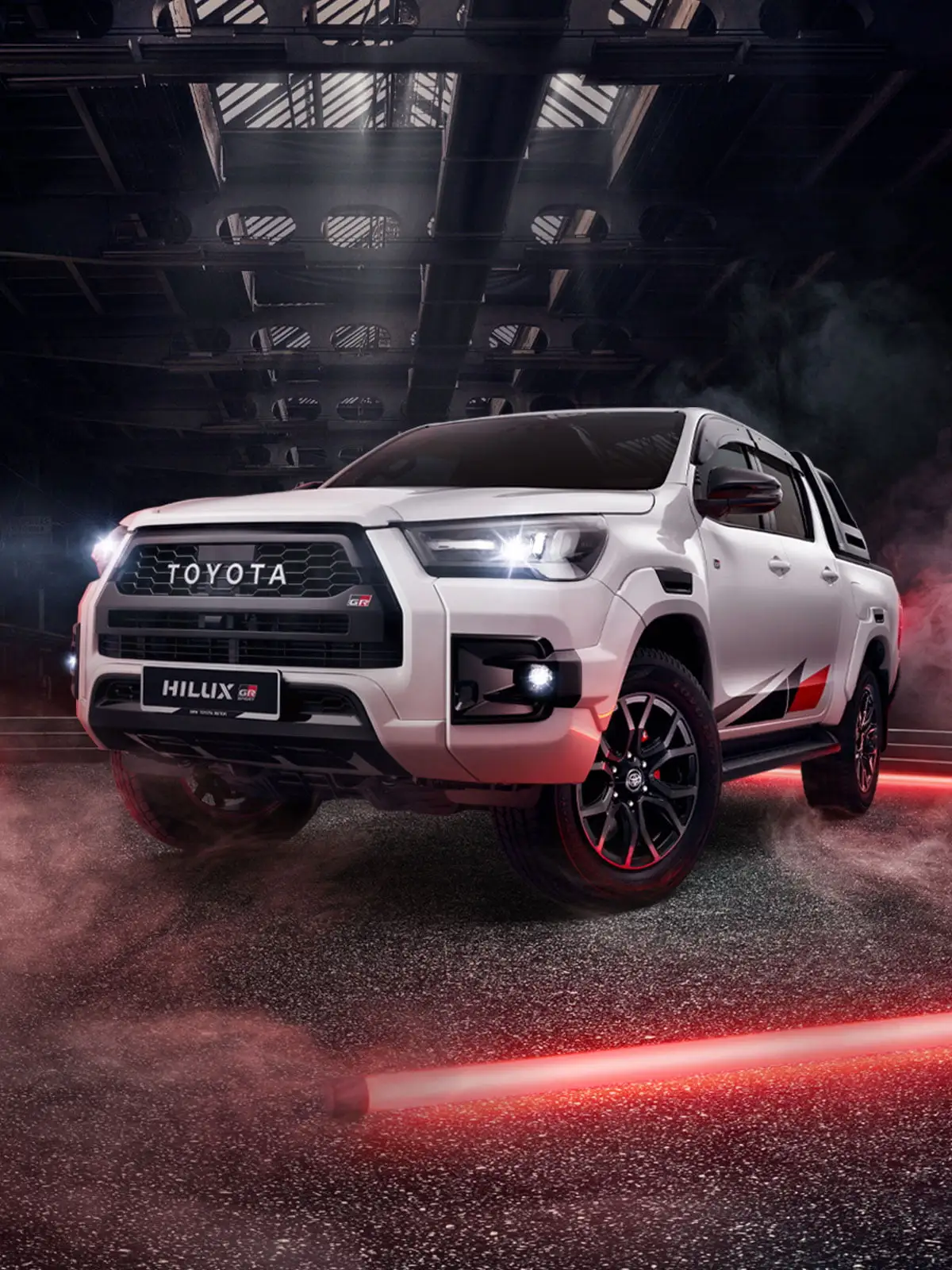 White Toyota Hilux GR Sport pickup truck in industrial warehouse with dramatic red lighting and performance styling