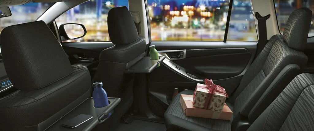 Toyota Innova spacious second-row interior featuring reclining seats, armrest with cup holders, and city view