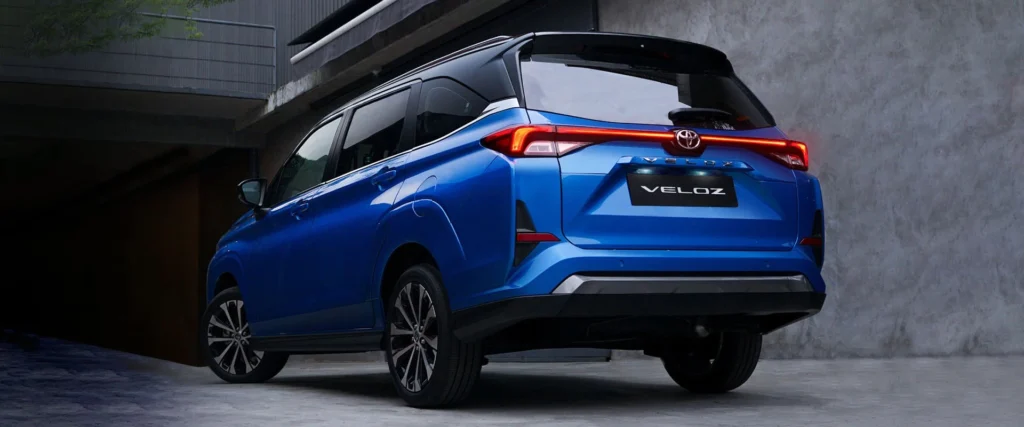 Toyota Veloz blue back angle view with illuminated red taillights against contemporary architecture