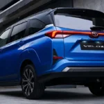 Toyota Veloz blue back angle view with illuminated red taillights against contemporary architecture