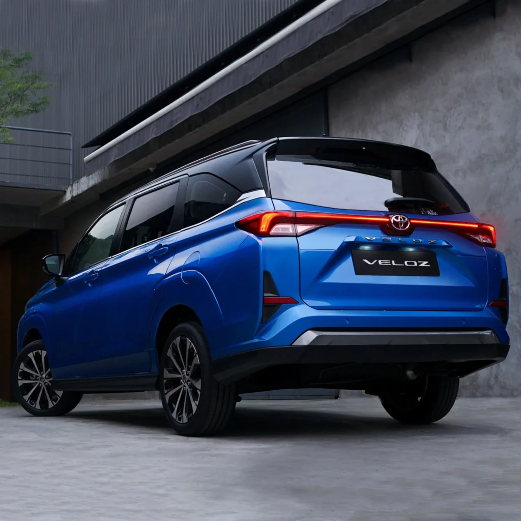 Toyota Veloz blue back angle view with illuminated red taillights against contemporary architecture