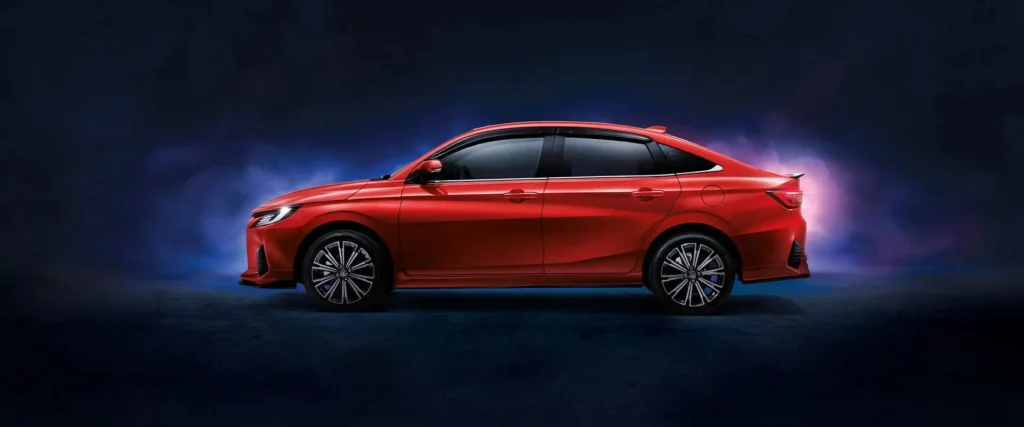 Red Toyota Vios sedan side profile with dramatic studio lighting showcasing sleek modern design and alloy wheels