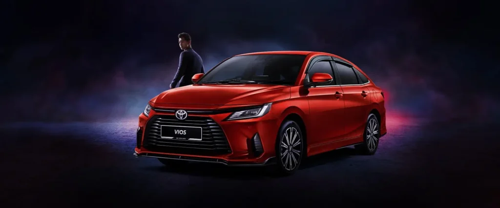 Red Toyota Vios sedan with person standing beside vehicle in atmospheric studio setting with blue lighting