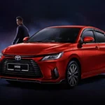 Red Toyota Vios sedan with person standing beside vehicle in atmospheric studio setting with blue lighting