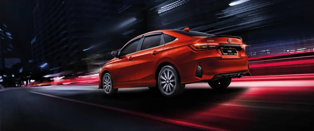 Toyota Vios red car back angle with illuminated taillights driving through city environment at night