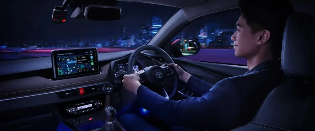 Driver in Toyota Vios interior with touchscreen navigation display while driving through city at night