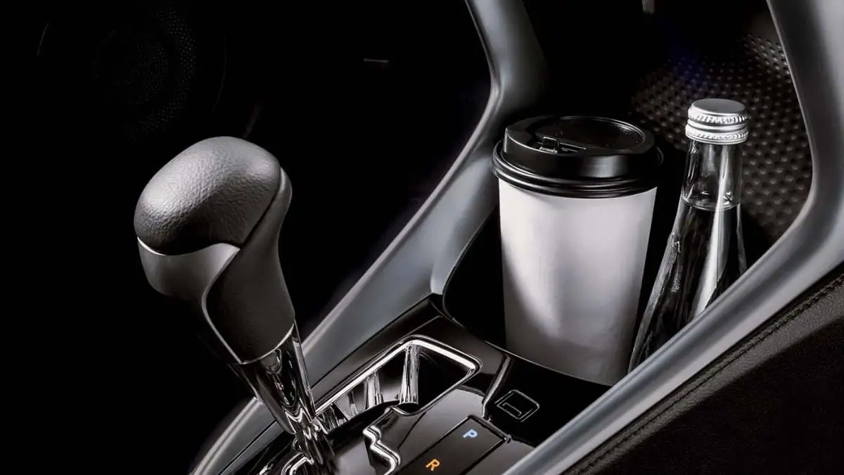 Car center console cup holders with white travel mug and glass bottle in premium interior setting