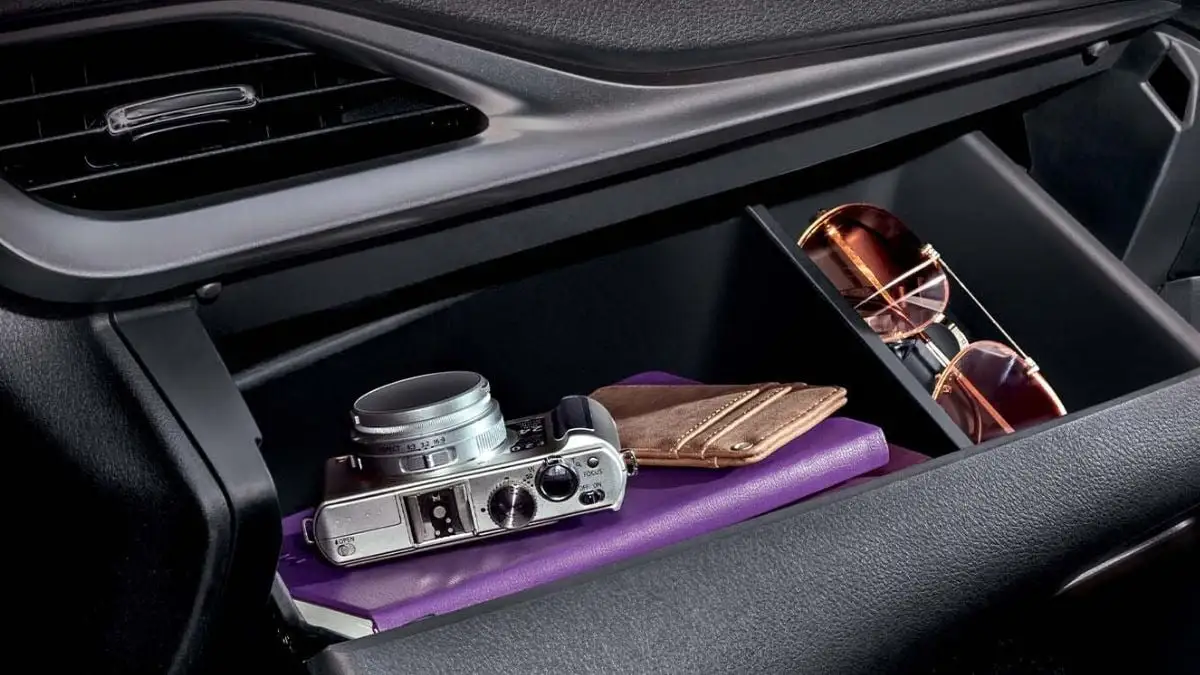 Car dashboard storage compartment containing vintage camera, leather wallet, sunglasses and purple notebook