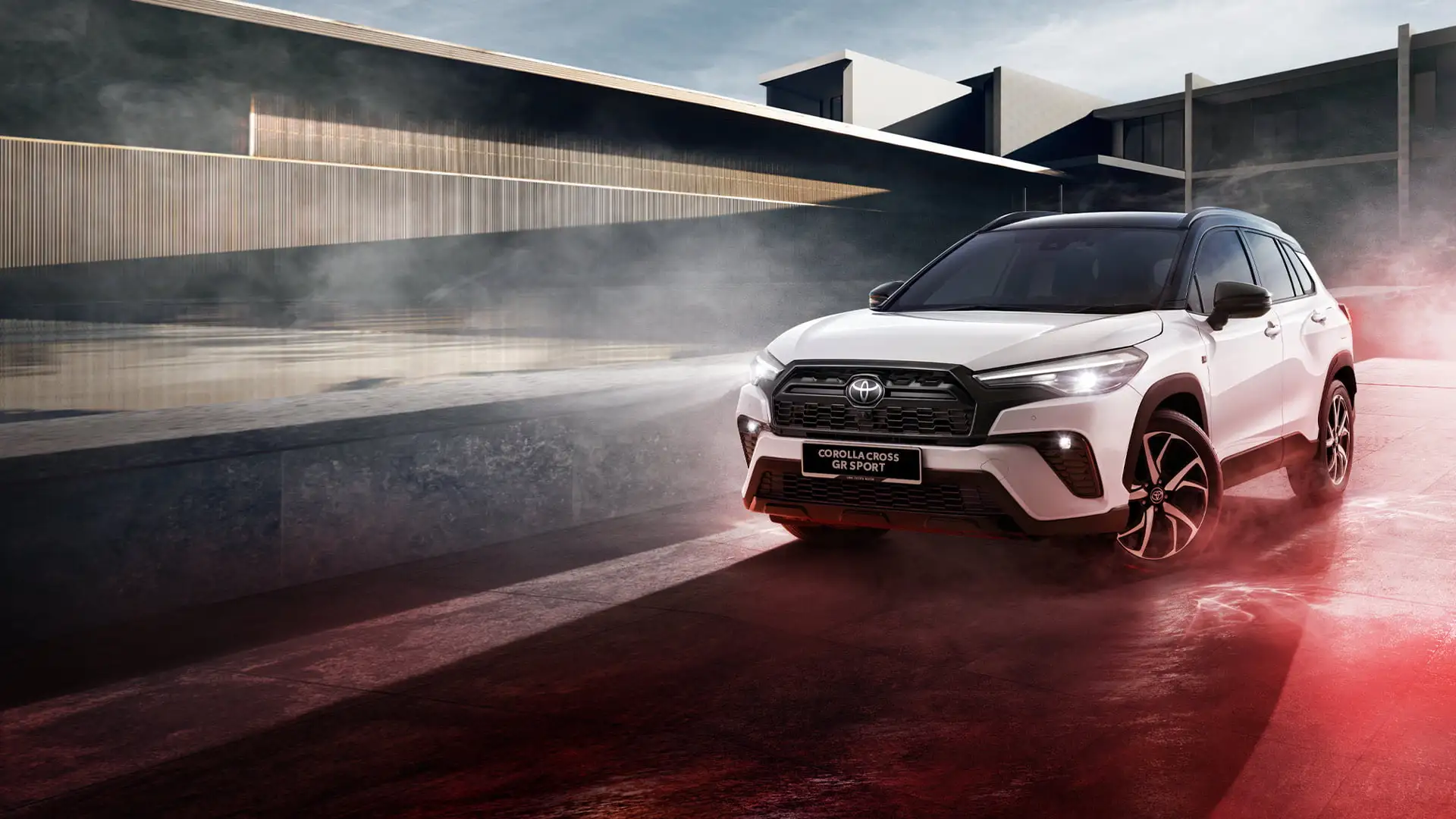 Toyota Corolla Cross GR Sport on reflective surface with modern architecture and dramatic lighting effects