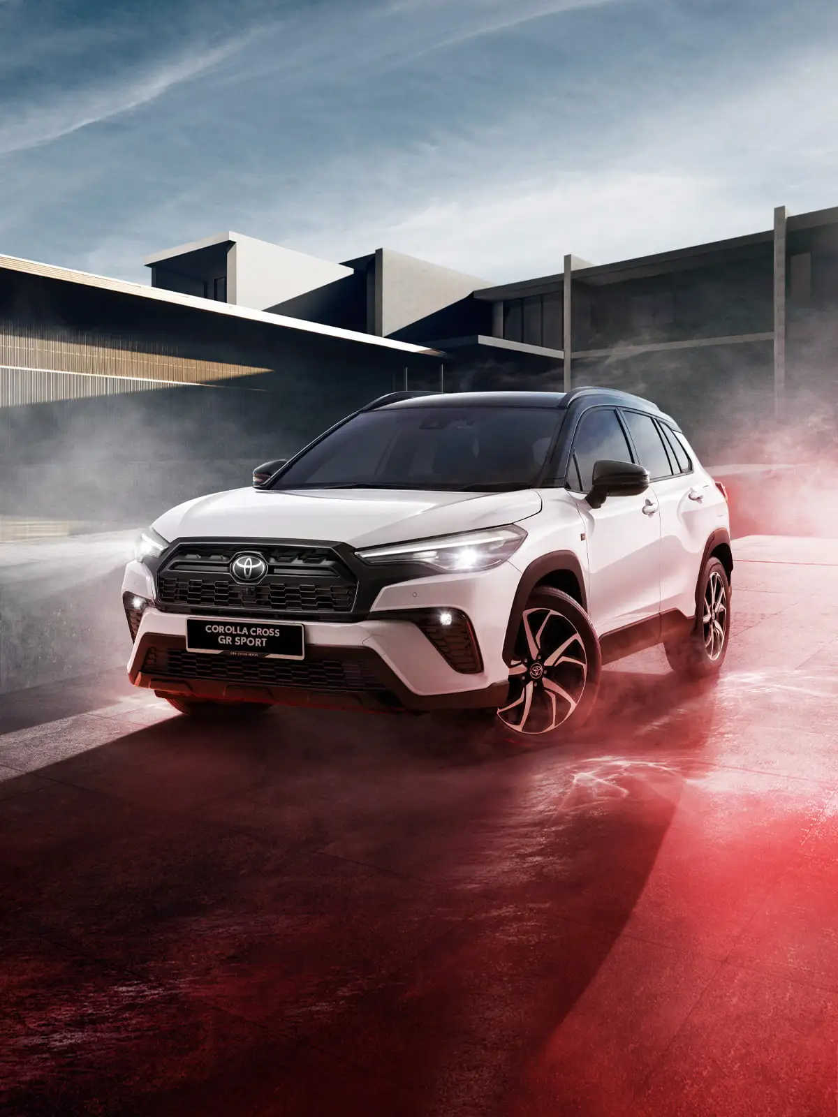 Toyota Corolla Cross GR Sport on reflective surface with modern architecture and dramatic lighting effects