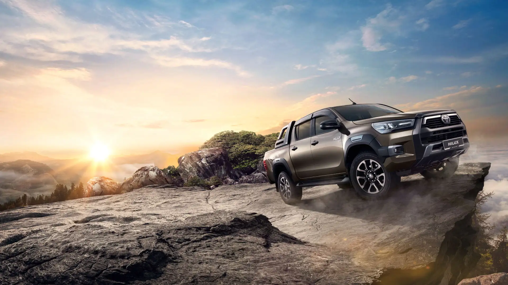 Toyota Hilux double cab showcasing off-road capability with alloy wheels on challenging rocky outcrop at golden hour