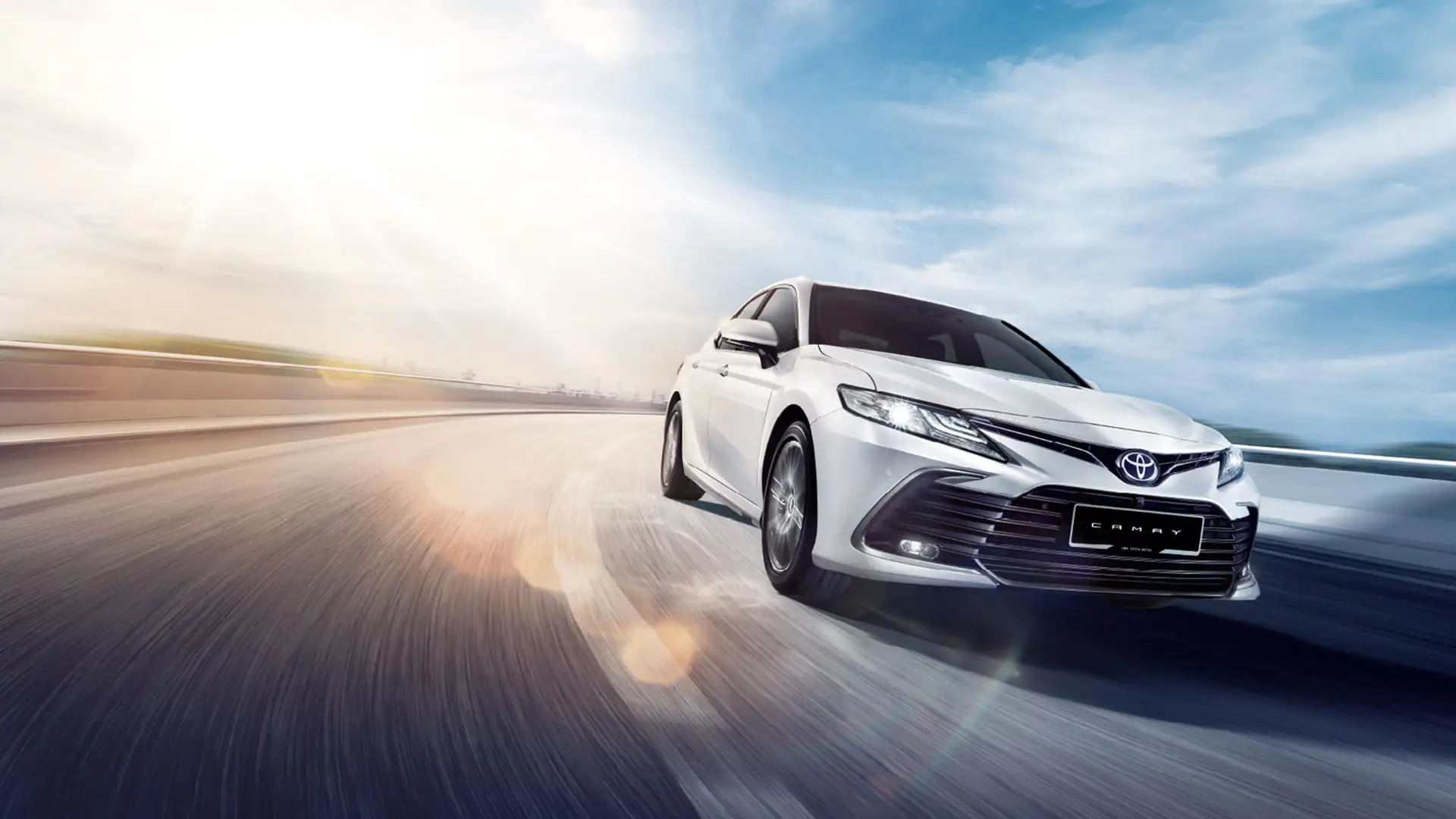 White Toyota Camry sedan driving on highway at sunset with motion blur effect and dramatic sky background