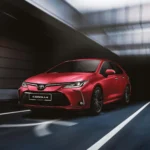 Red Toyota Corolla sedan parked in modern underground garage with dramatic lighting and concrete architecture