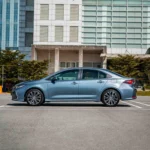 Side angle of Toyota Corolla parked outside modern office building with glass facade and urban landscaping