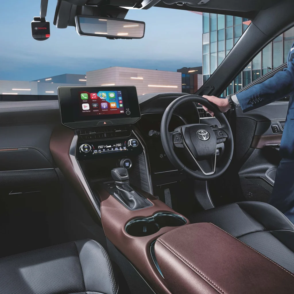 Toyota Harrier dashboard view showing driver operating touchscreen display with smartphone connectivity apps