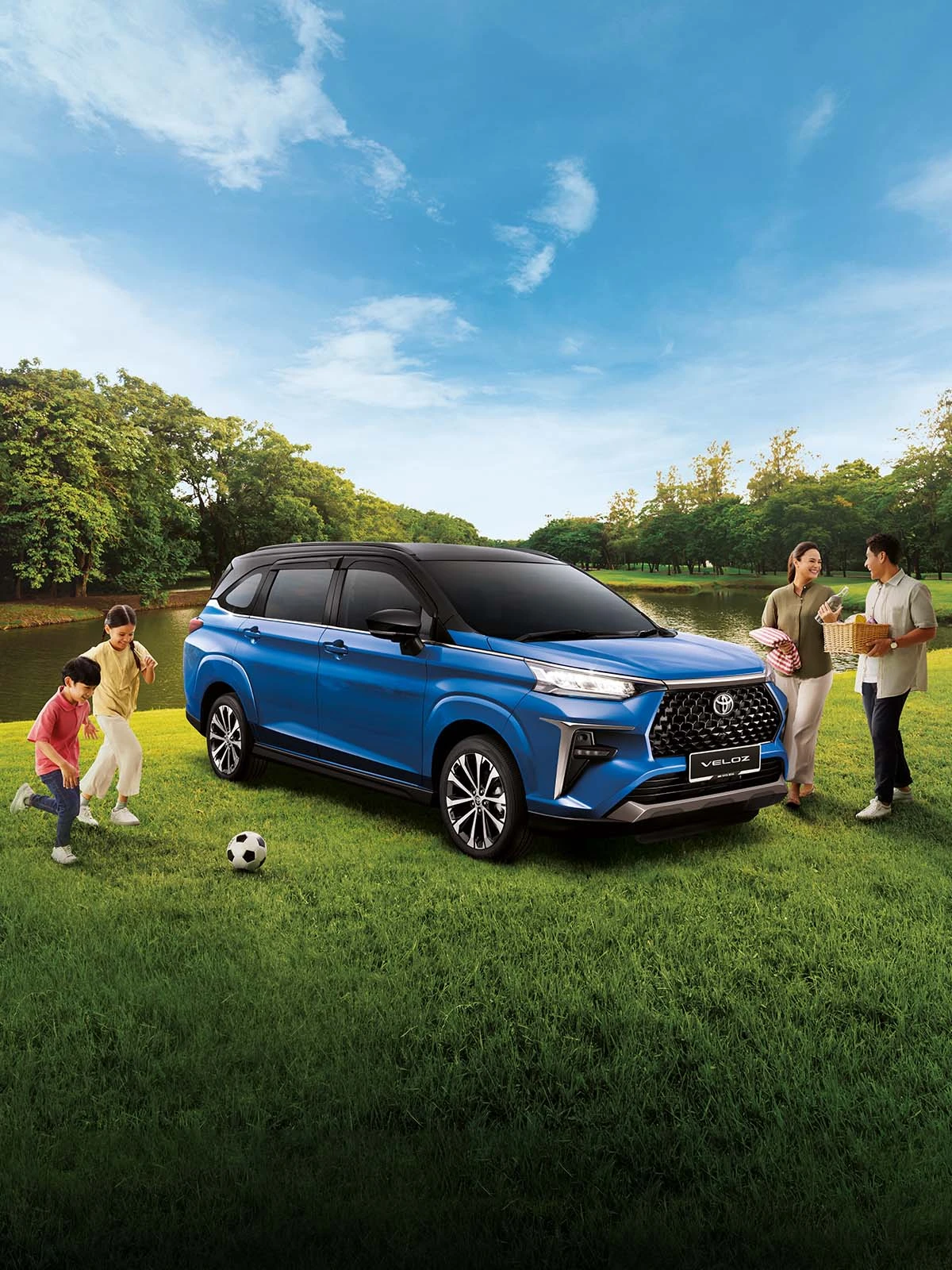 Toyota Veloz blue parked on green grass beside lake with family enjoying outdoor picnic and children playing