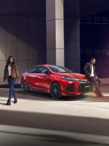 Red Toyota Vios sedan with stylish couple posing near modern glass building during golden hour lighting