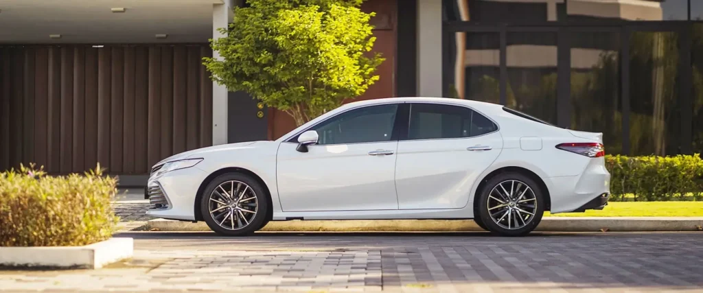Side angle of Toyota Camry showing sleek design lines against modern house and green landscaping background