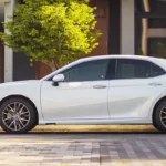 Side angle of Toyota Camry showing sleek design lines against modern house and green landscaping background