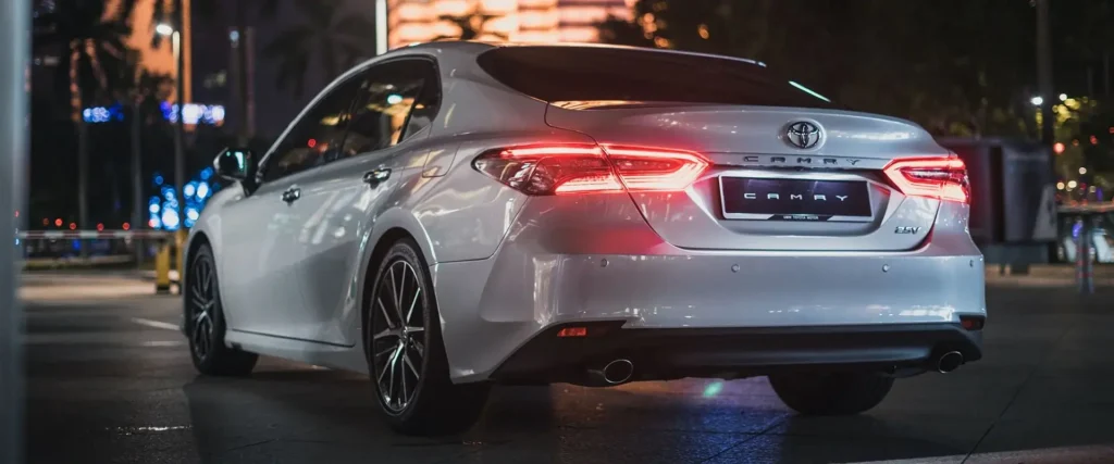 Nighttime shot of Toyota Camry from behind showing LED brake lights and modern city backdrop