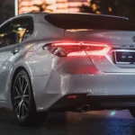 Nighttime shot of Toyota Camry from behind showing LED brake lights and modern city backdrop
