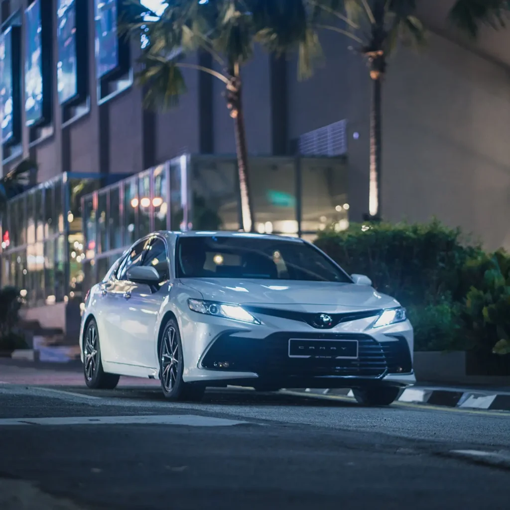Toyota Camry positioned on city road during evening hours with metropolitan skyline behind