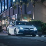 Toyota Camry positioned on city road during evening hours with metropolitan skyline behind